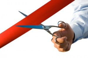 hand holding scissors cutting red ribbon