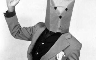 Man Dressed In Suit Wearing a Paper Bag With Holes For Eye and Mouth