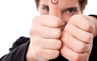 Man with spiked hair has one thumb up one down, both with sharpie faces on them.