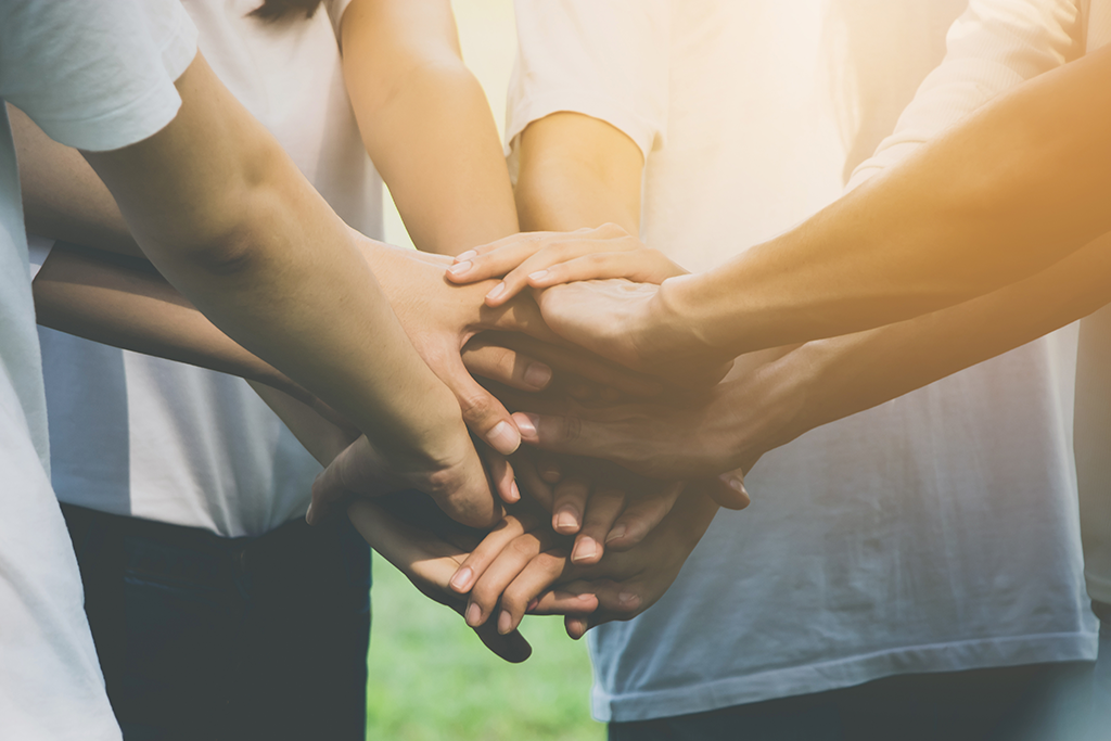 4 people in a circle hands in center - group effort