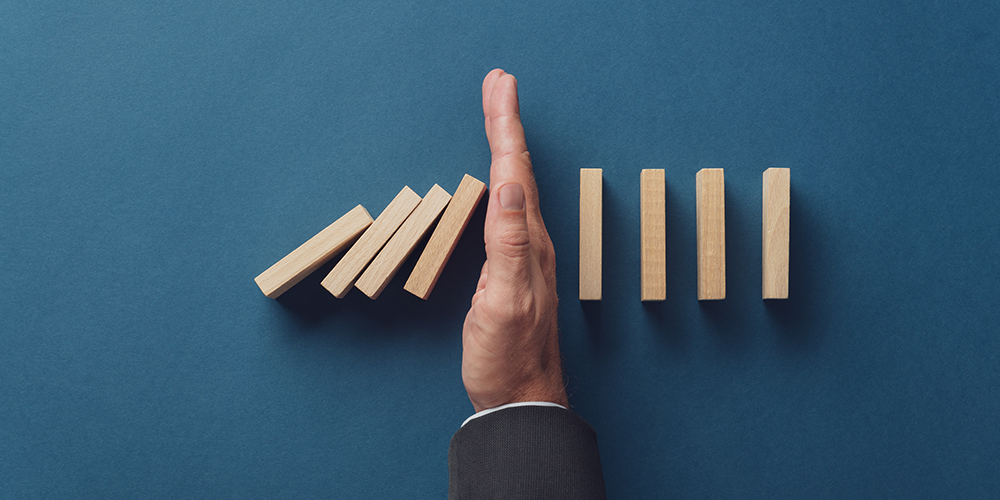 hand stopping dominoes from knocking down other dominoes