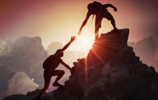 one person on top of a boulder helping another person up