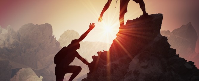 one person on top of a boulder helping another person up