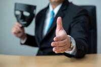A business man with a black mask covering the insincerity of doing business together.Corruption concept.