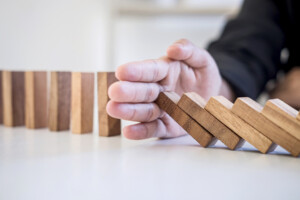 Risk and Strategy in Business, Image of hand stopping falling collapse wooden block dominoes effect from continuous toppled block, prevention and development to stability.