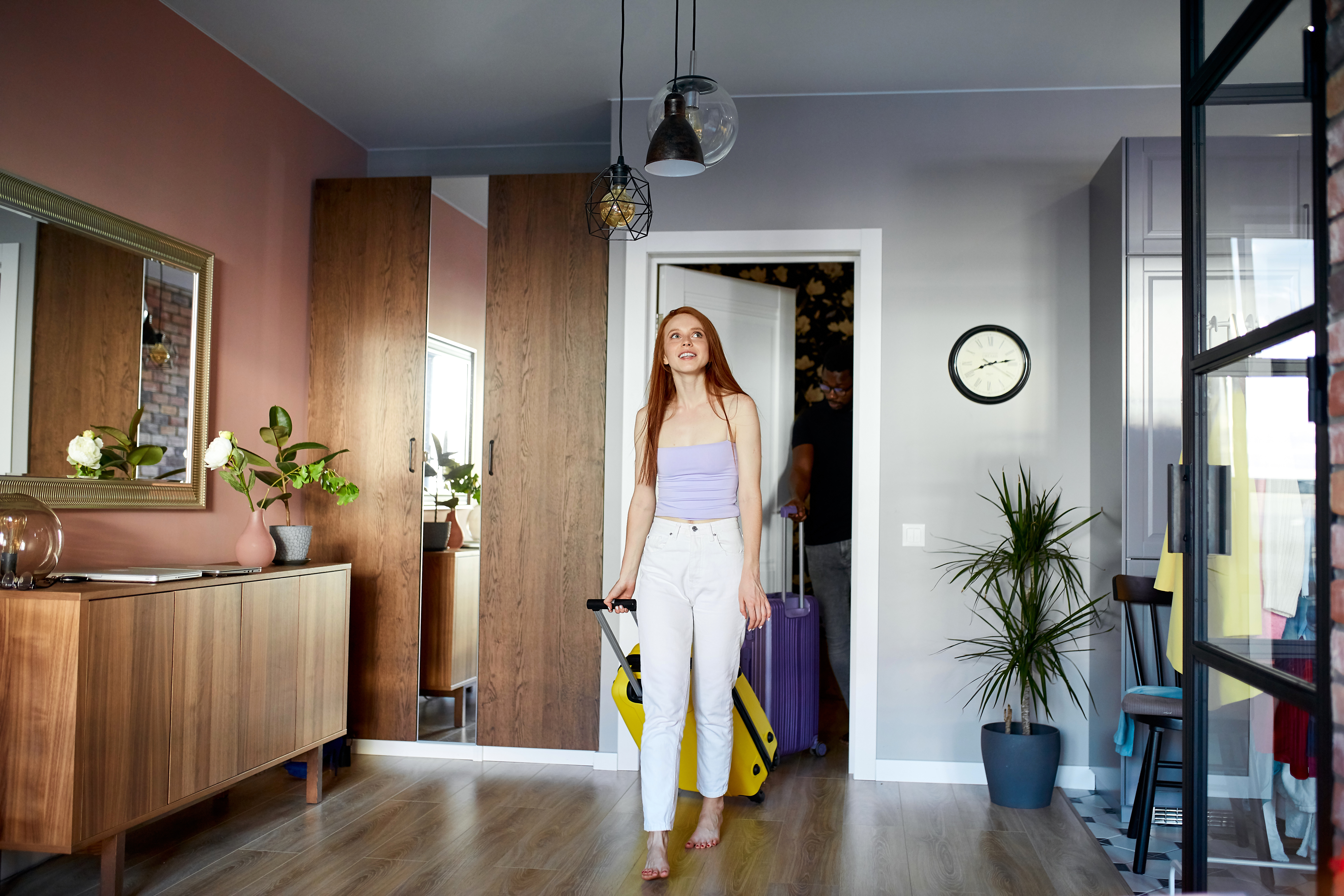 young redhead woman and african man in new house, woman is surprised with beauty of room, they carry suitcases in hands