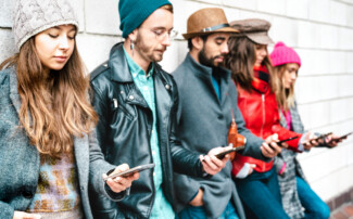 Side view of milenial guys and girls using mobile smartphone - People addicted by smart phone - Life style concept with always connected teenagers - Vivid filter with focus on first left cellphone